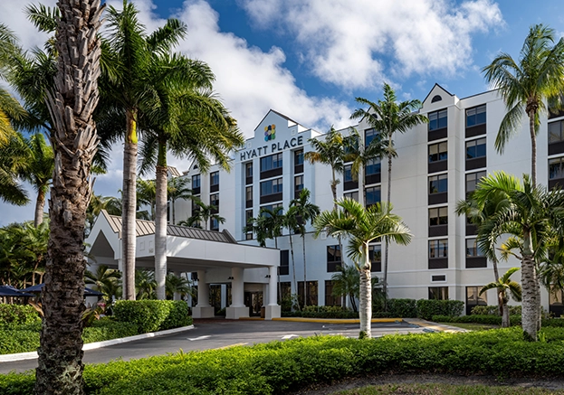 Hyatt Place hotel exterior with palm trees and covered entrance under blue sky.